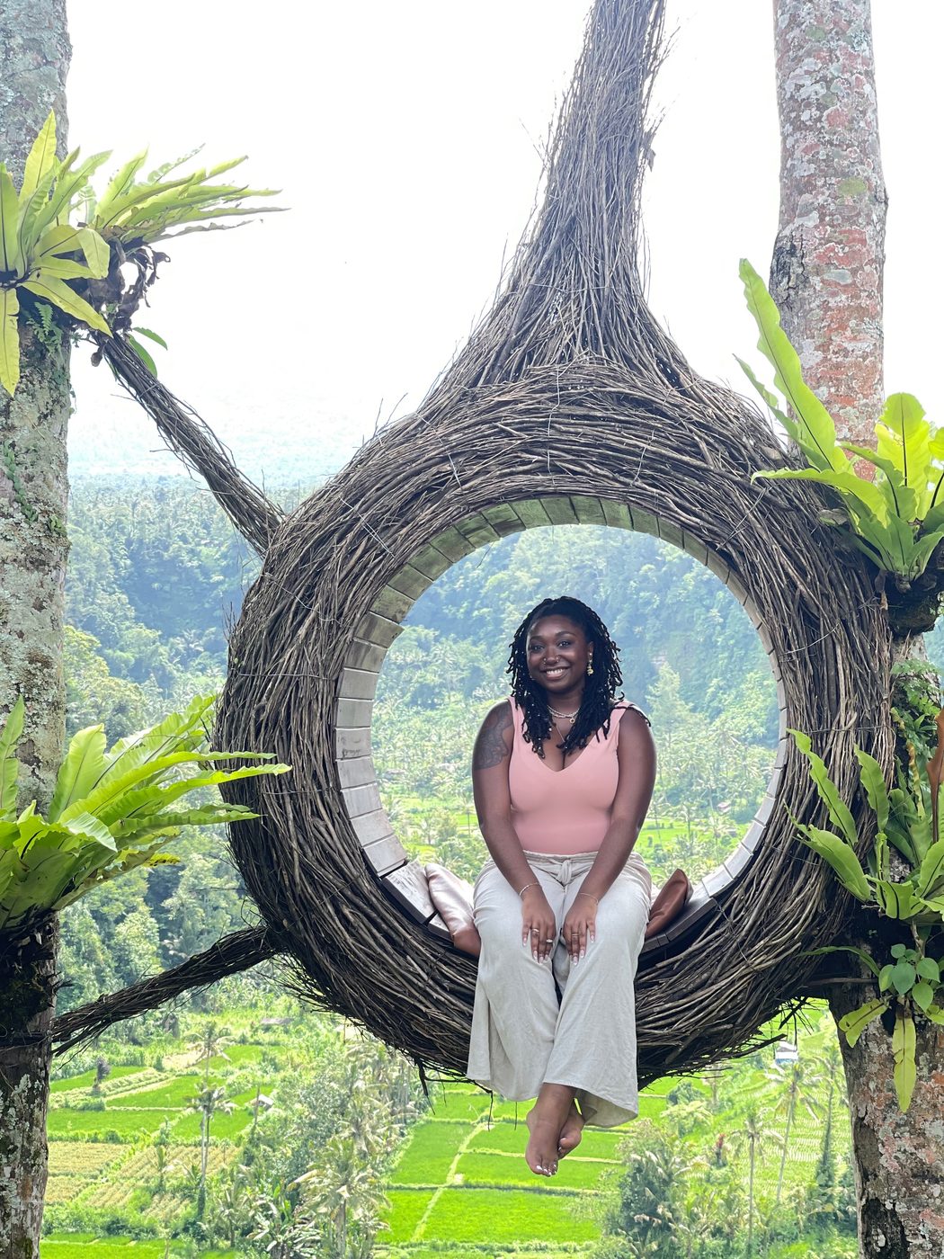 Ashleigh sitting inside a woven nest swing above green rice terraces