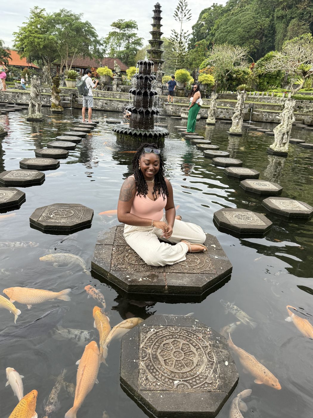 Ashleigh seated cross-legged on a stepping stone in a koi pond